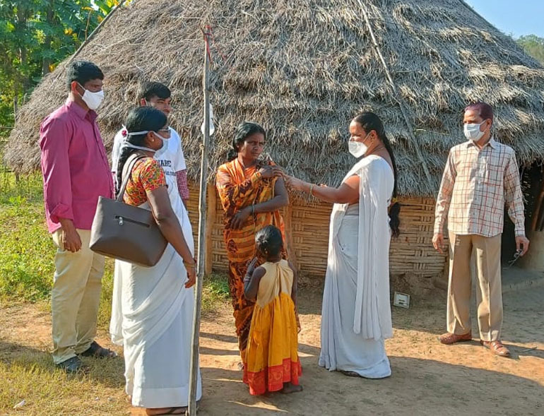 Health workers vaccinating a villager outside a thatched home